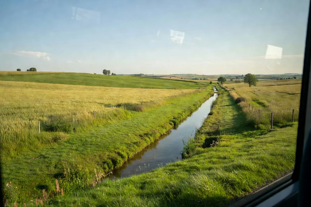 View of green fields and a canal passing by a coach window in daylight