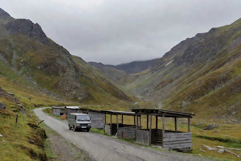 Small coach at a roadside stop in a northern valley with wooden stalls nearby